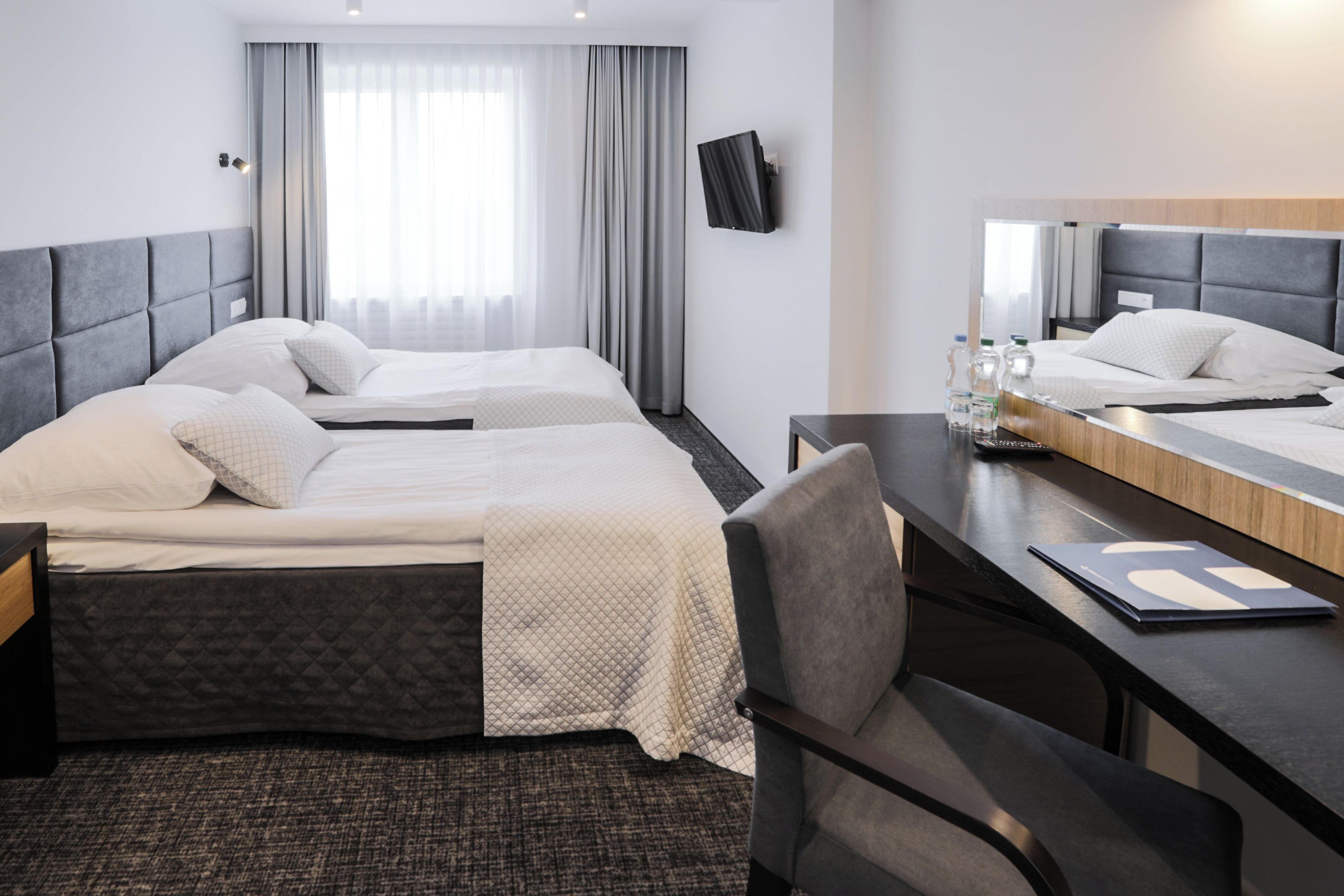 Habitación de hotel con dos camas, un escritorio, una silla, un televisor y un ventanal con cortinas.