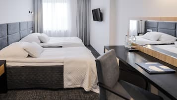Habitación de hotel con dos camas, un escritorio, una silla, un televisor y un ventanal con cortinas.