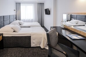 Habitación de hotel con dos camas, un escritorio, una silla, un televisor y un ventanal con cortinas.