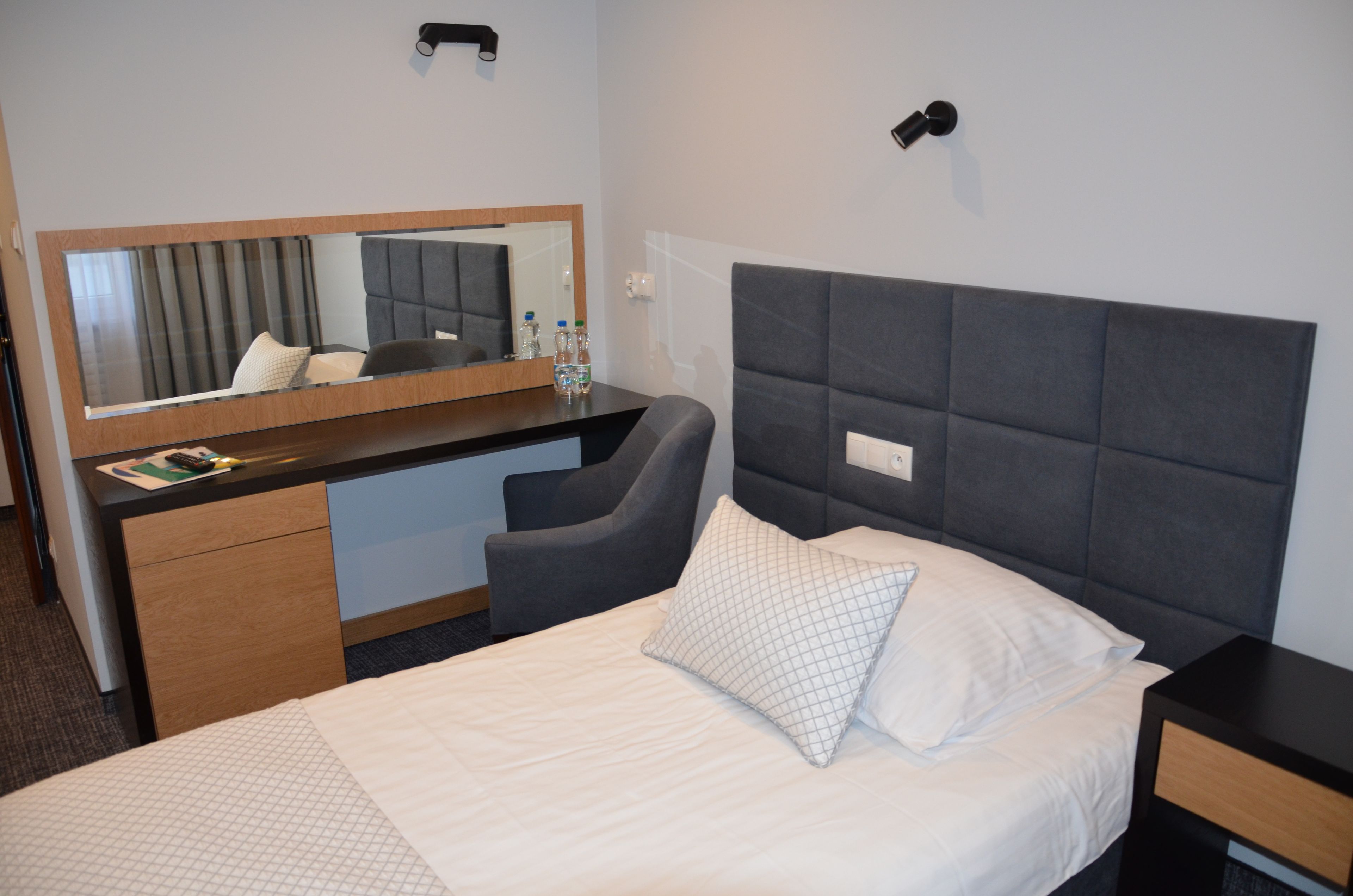 A hotel room with a bed, a desk, a chair, a mirror, and a nightstand.