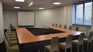 Ett konferensrum med ett långt bord, stolar, en projektorduk och ett fönster med persienner.