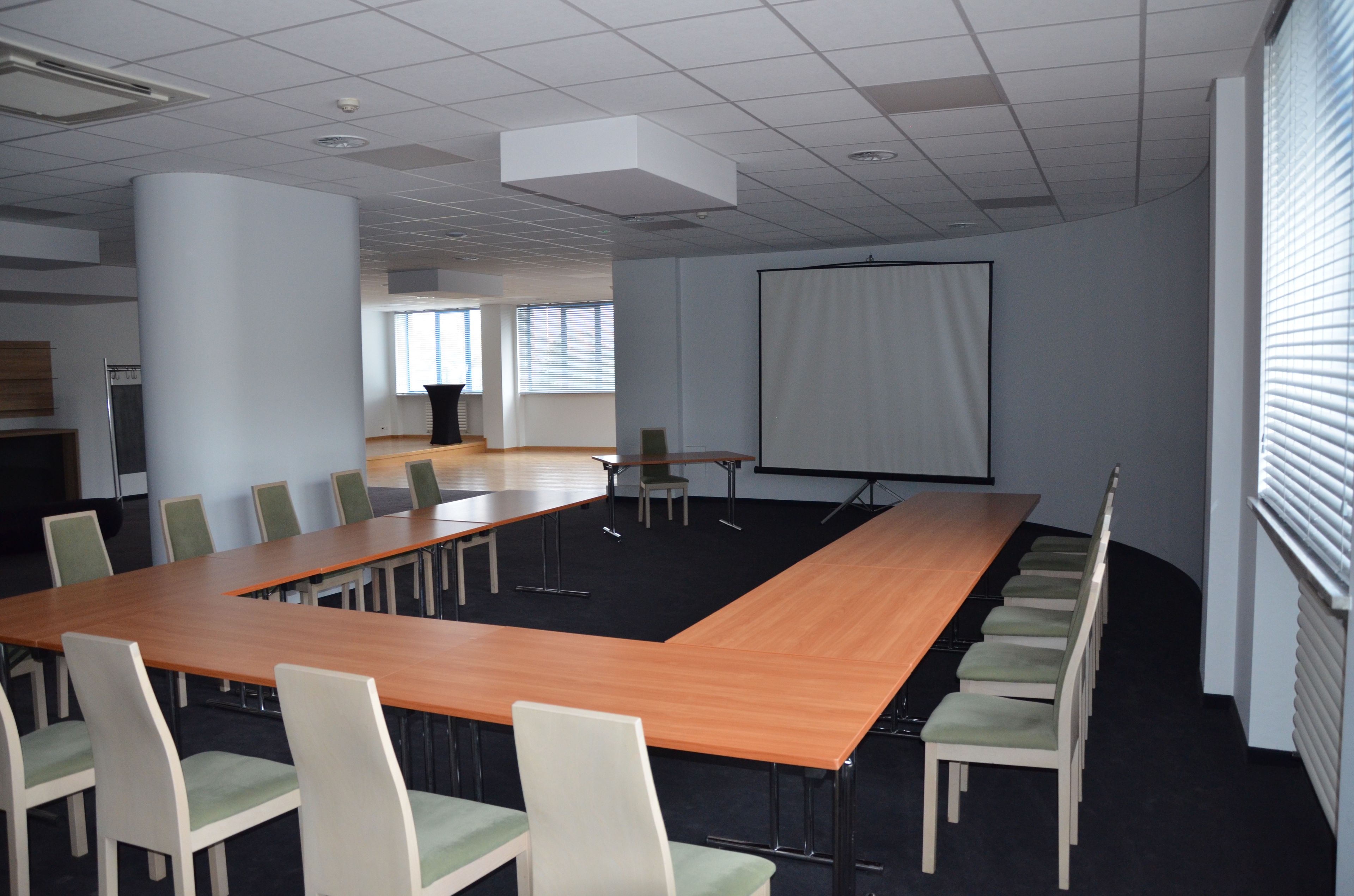 A conference room with a long table, chairs, a projector screen, and a large window.