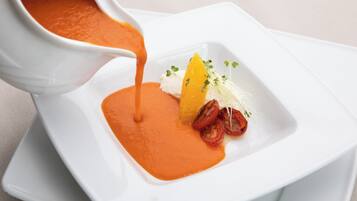 Prato branco quadrado com molho laranja liso, uma fatia de laranja, um pedaço de alimento branco e alguns enfeites verdes.