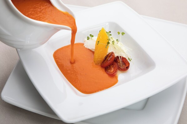 Un plato cuadrado blanco con salsa anaranjada, una rodaja de naranja, un trozo de comida blanca y un poco de guarnición verde.