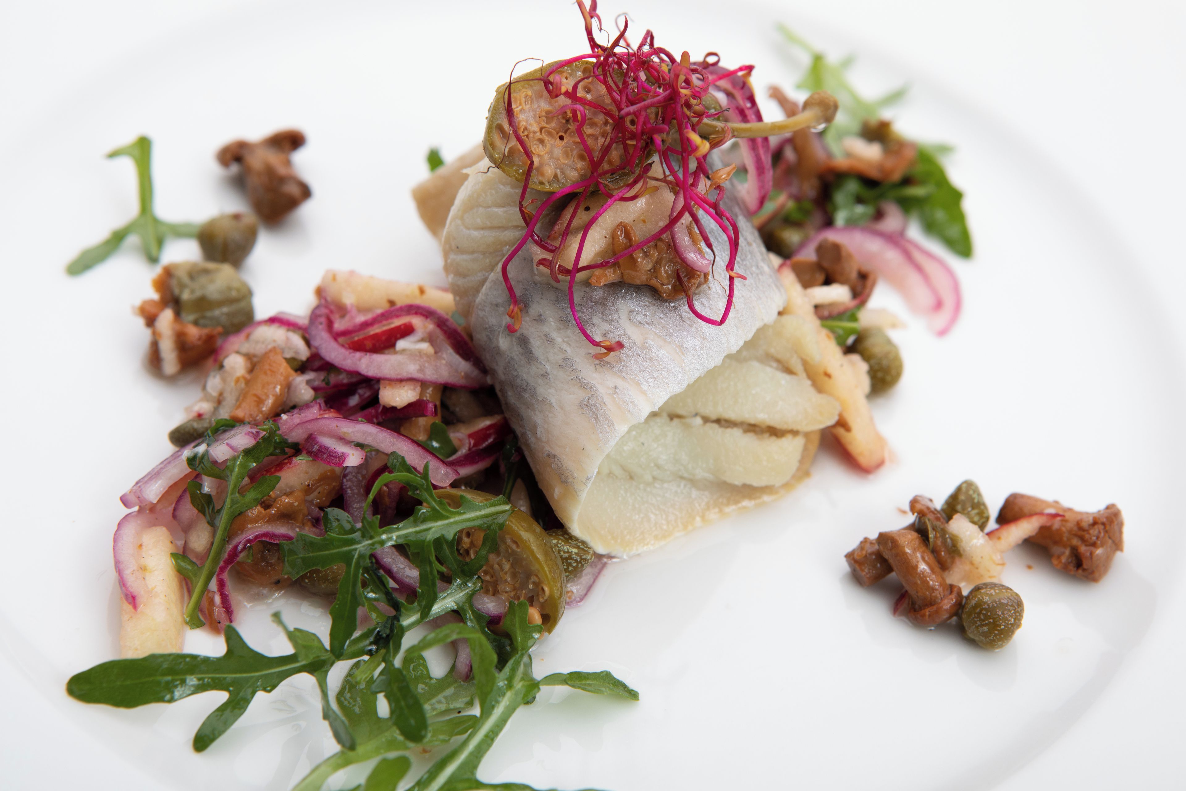 A plate of food with a fish fillet, greens, and capers.