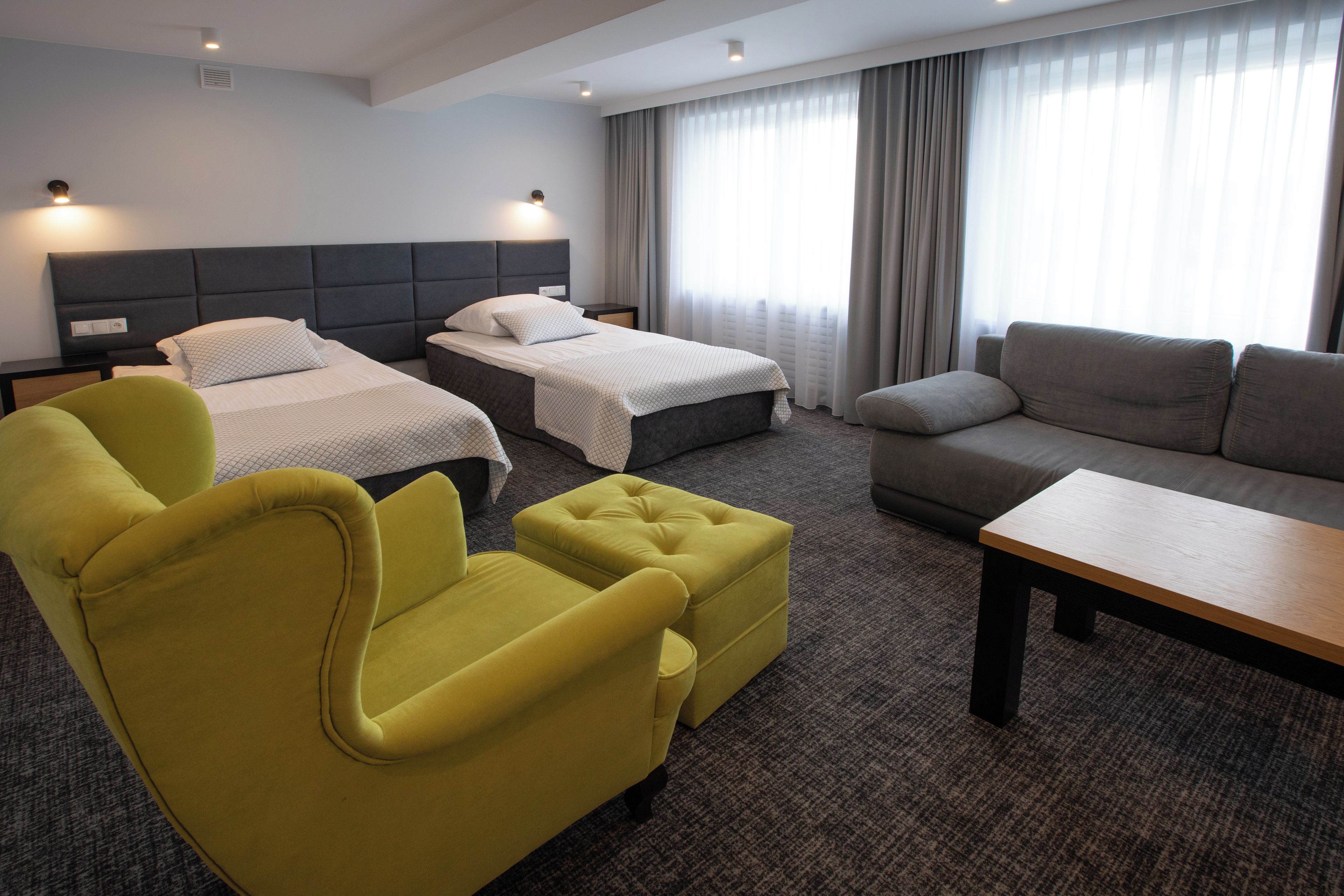 A hotel room with two beds, a yellow armchair, a grey sofa, and a wooden table.