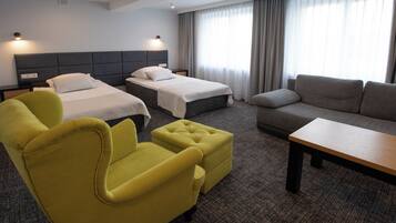 A hotel room with two beds, a yellow armchair, a grey sofa, and a wooden table.