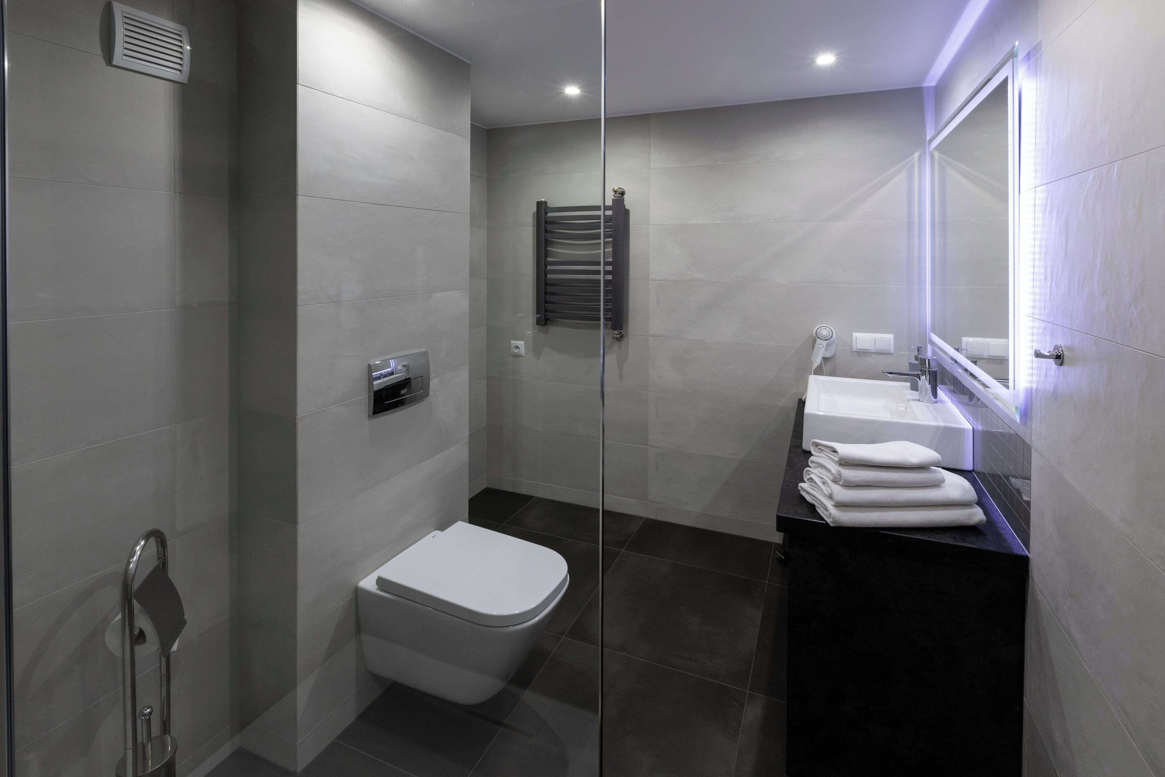 Ein modernes Badezimmer mit Duschkabine aus Glas, Toilette in Weiß, Handtuchhalter und Waschbecken mit Spiegel.