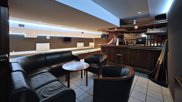 A bar area with leather seating, a counter, and a television screen. - Hotel Sport (Belchatow)