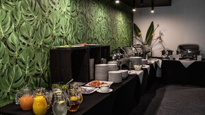 A buffet setup with a green leaf-patterned wall, a variety of dishes, and a coffee station.