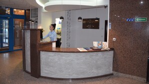 A hotel reception desk with a receptionist, a sign indicating 'HOTEL SPREE', and a directional sign pointing left.