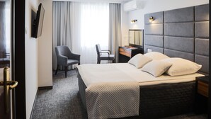 A hotel room with a large bed, a desk, a chair, and a TV mounted on the wall.