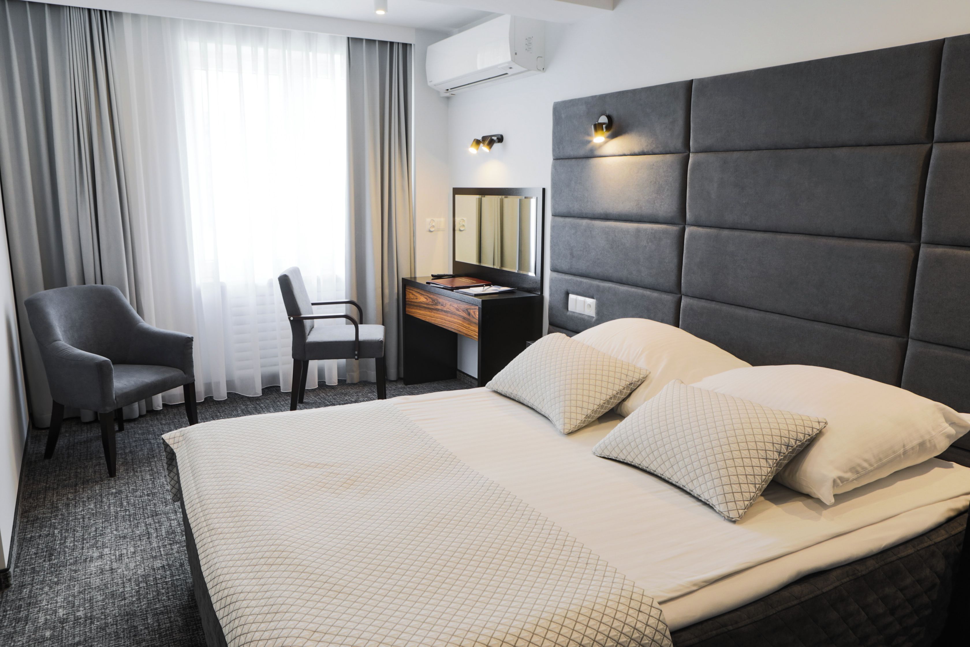 Una habitación de hotel con una cama grande, un escritorio con silla, un espejo y una ventana con cortinas.