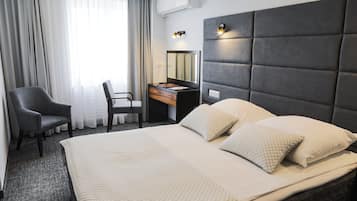Una habitación de hotel con una cama grande, un escritorio con silla, un espejo y una ventana con cortinas.