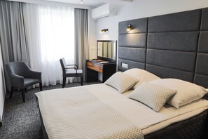 Una habitación de hotel con una cama grande, un escritorio con silla, un espejo y una ventana con cortinas.