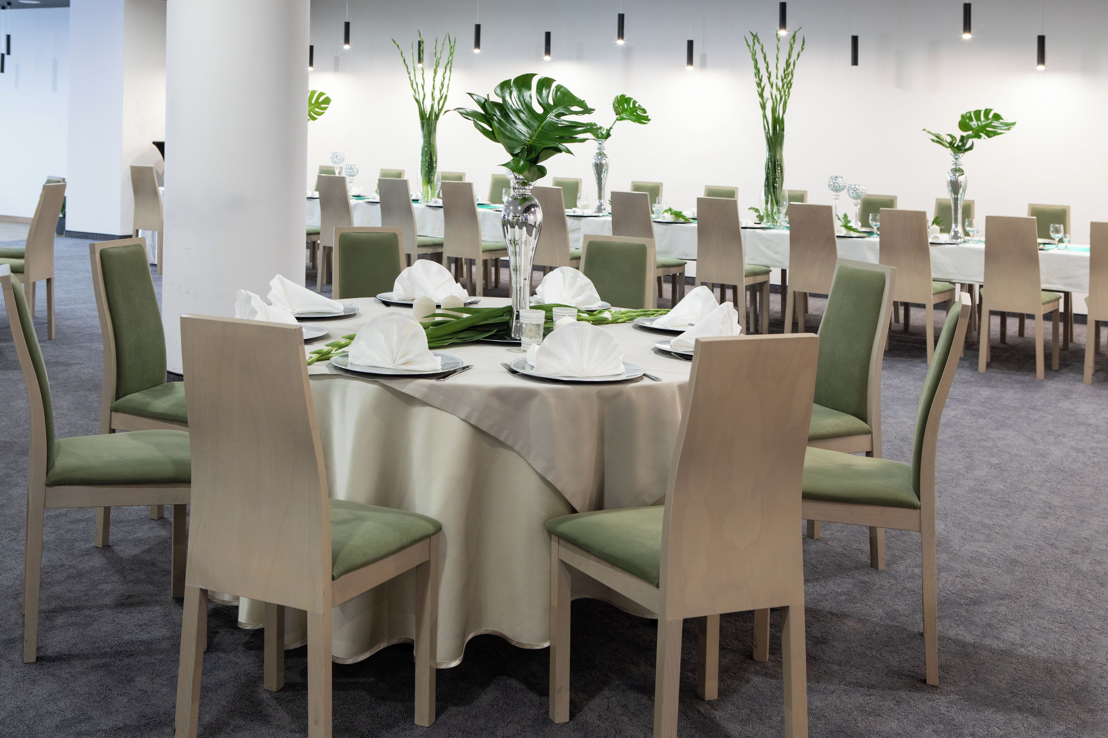 A conference room with round tables, green upholstered chairs, and white tablecloths.