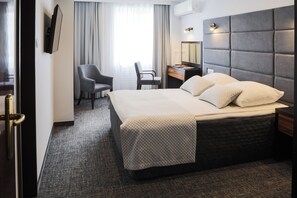 Habitación de hotel con una cama grande, un escritorio, una silla y un televisor montado en la pared.