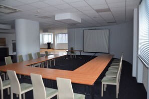 A conference room with a long table, chairs, a projector screen, and a large window. - Hotel Sport (Belchatow)
