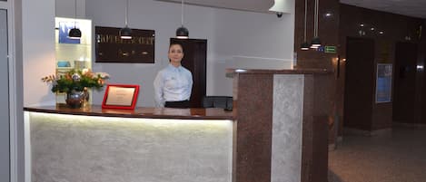 A hotel reception desk with a modern design, a framed certificate, and a decorative vase.