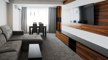 Ein modernes Hotelzimmer mit Ecksofa, einem flachbildfernseher an einer Holzvertäfelung, einem Essbereich mit Tisch und Stühlen sowie einem großen Fenster mit Vorhängen.