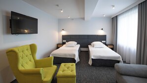 A hotel room with two single beds, a yellow armchair, a grey sofa, and a flat-screen TV mounted on the wall. - Hotel Sport (Belchatow)