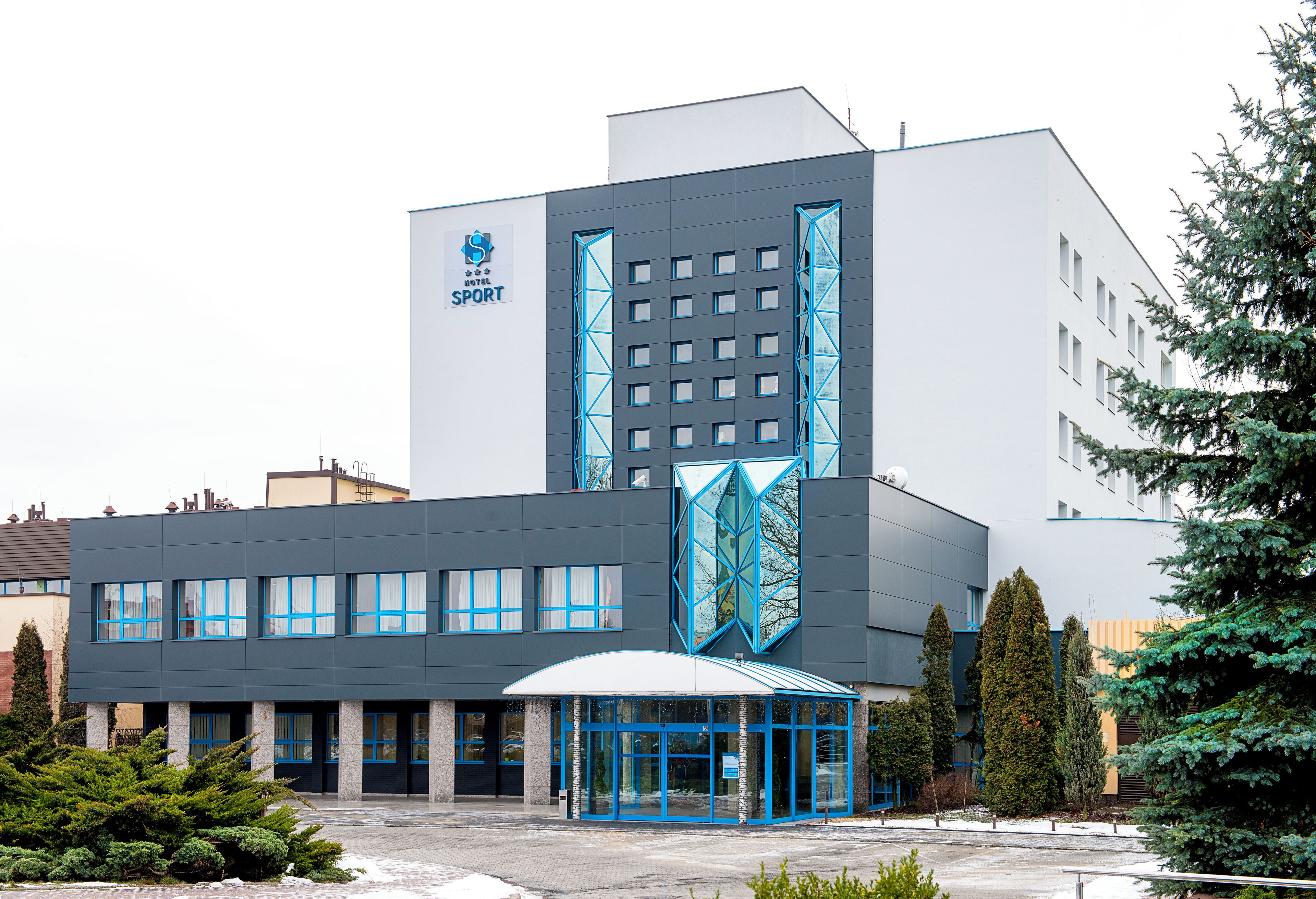 En modern hotellbyggnad med en tydlig logotyp, en överbyggd entré och en parkeringsplats.