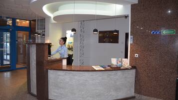 Een receptiebalie van een hotel met een receptionist, een bord met de tekst 'HOTEL SPREE' en een richtingwijzer die naar links wijst.