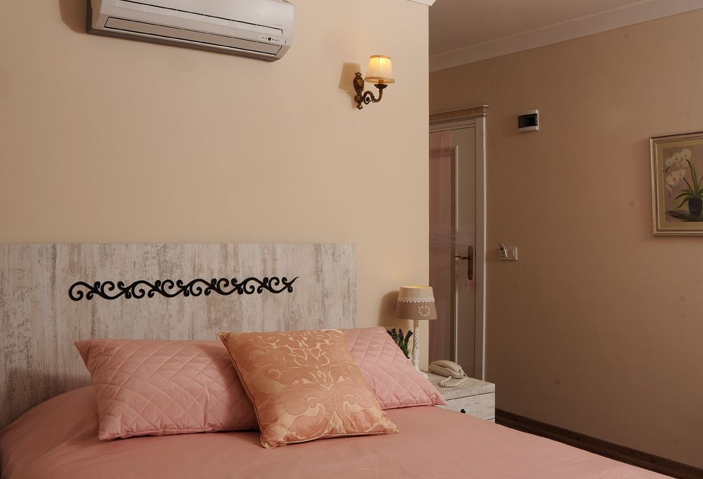 A bedroom with a bed, a nightstand, a lamp, an air conditioner, and a door.