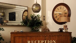 Un espace d’accueil avec un bureau en bois portant l’inscription « RÉCEPTION », une grande horloge ronde fixée au mur, une lampe suspendue et un miroir au-dessus du bureau.