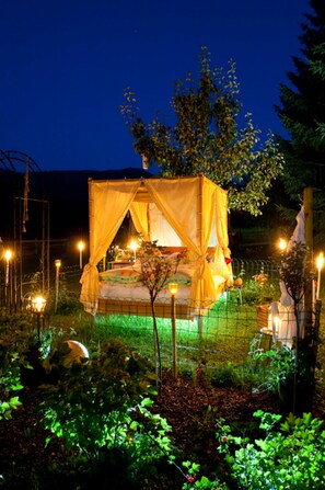 A secluded outdoor tent with a canopy, surrounded by a garden with various plants and a fence. - die Unterbergerin (Dorfgastein)