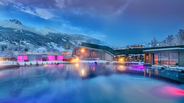 Un hotel moderno con piscina, rodeado de montañas nevadas e iluminado por luces de colores.