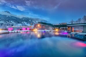 A modern hotel with a pool, surrounded by snow-covered mountains and illuminated by colorful lights. - die Unterbergerin (Dorfgastein)