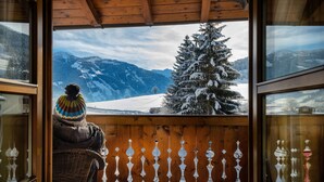 Un balcón de madera con vistas a montañas nevadas y un árbol.