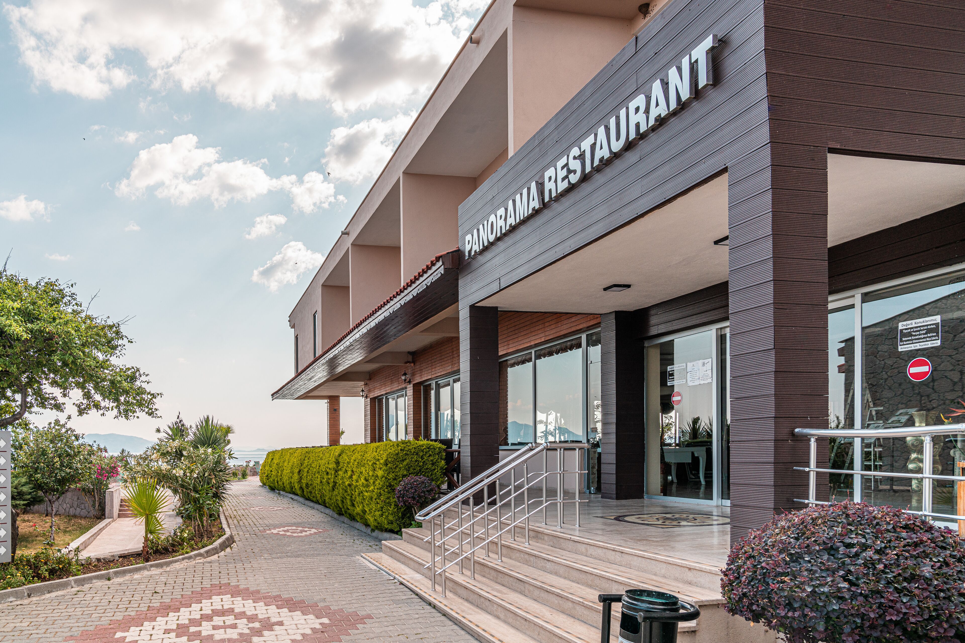 Un bâtiment moderne avec une enseigne indiquant « RESTAURANT PANORAMA » et un escalier menant à l’entrée.