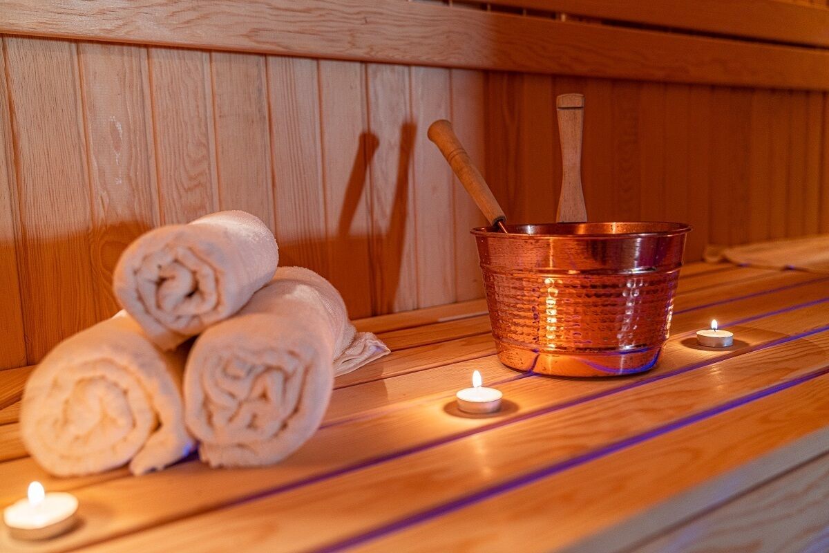 Een houten sauna bank met opgerolde handdoeken en een koperen emmer.
