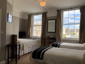 A bedroom with two beds, a desk, a chair, a TV, and large windows with curtains. - Harvey's Guesthouse (Dublin)