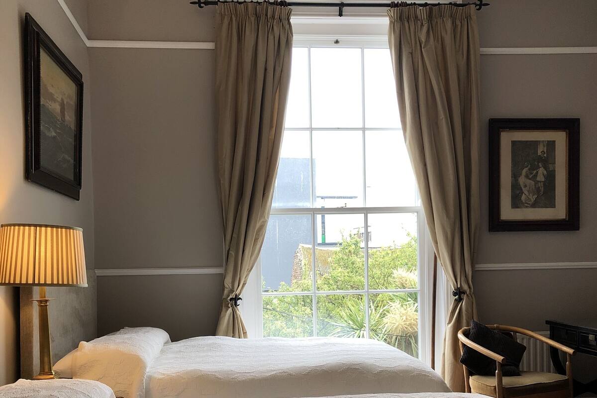 A hotel room with two beds, a desk, a chair, a lamp, and a window with curtains.