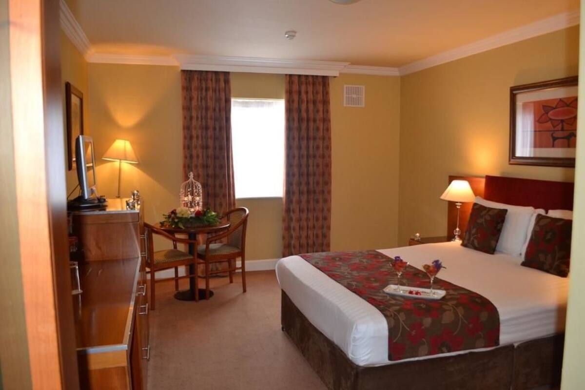 A hotel room with a bed, a desk, a chair, a lamp, and a window with curtains.