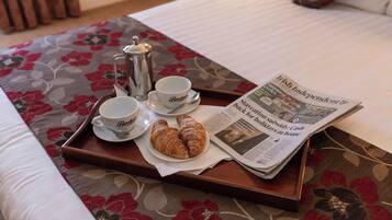 A tray with croissants, coffee cups, and a newspaper on a bed with floral bedding.