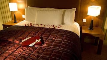 A hotel room with a large bed, two bedside lamps, and a red gift box on the bed.