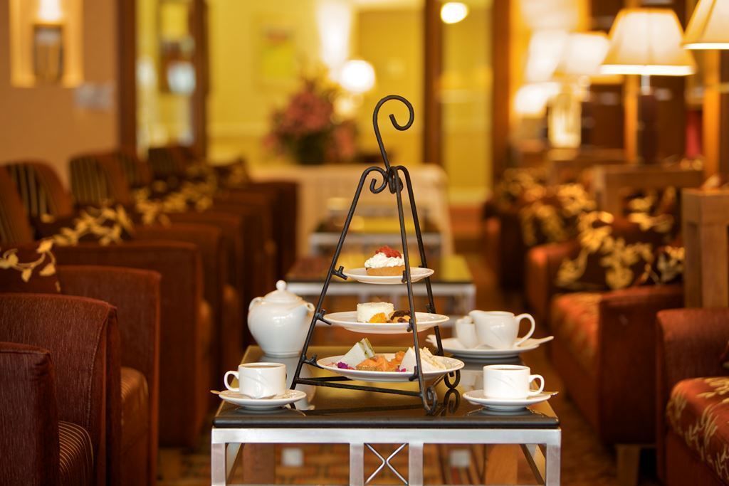Suporte de bandeja para chá em três níveis, com xícaras e pires sobre uma mesa em uma sala de jantar de hotel.