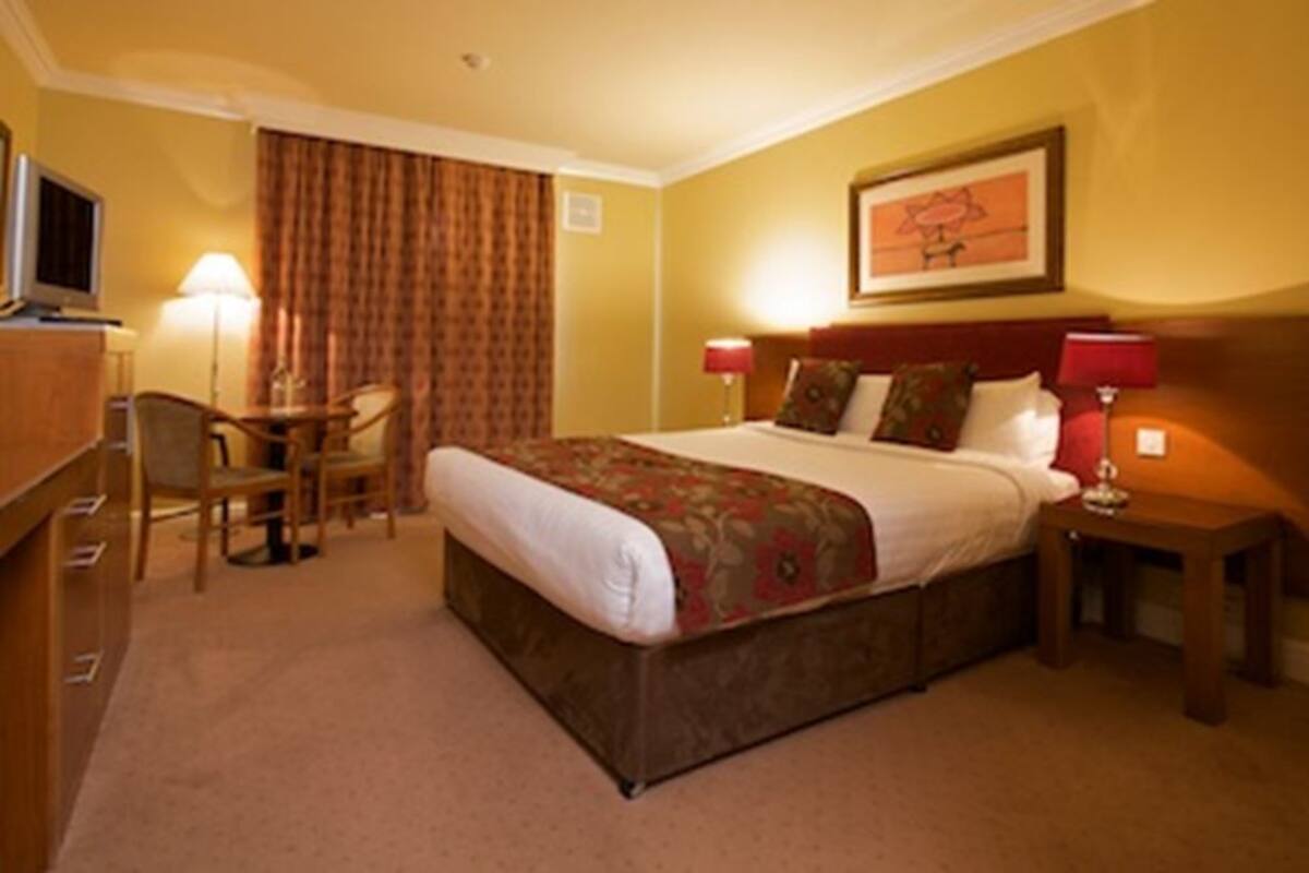 A hotel room with a bed, a desk, a chair, a TV, and a lamp.
