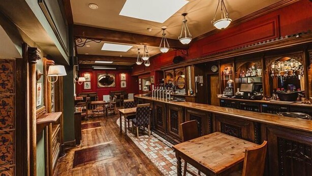 A bar with wooden furniture, a tiled floor, and a high ceiling with skylights. - Hamlet Court Hotel (Johnstown Bridge)
