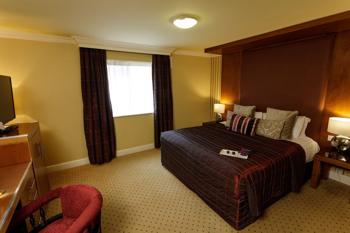 A hotel room with a large bed, a desk, a chair, and a window with curtains.