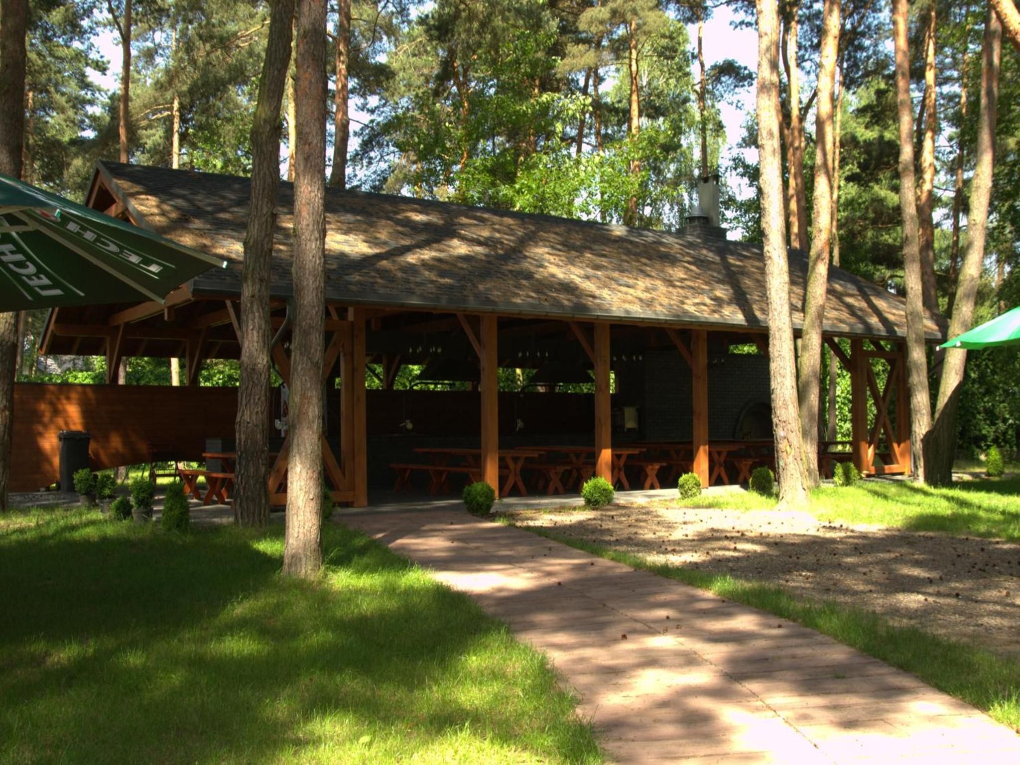 A wooden pavilion with a covered seating area, surrounded by trees and a gravel path.