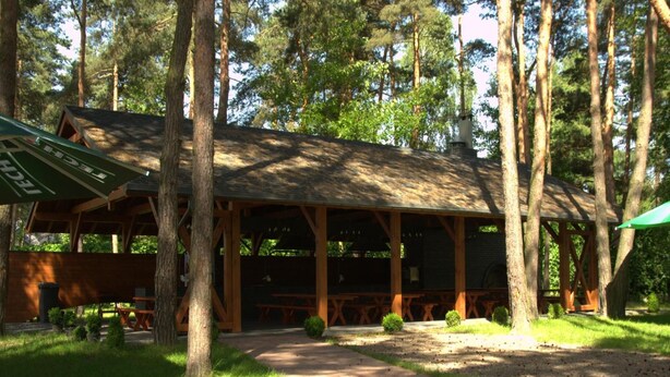 A wooden pavilion with a covered seating area, surrounded by trees and a gravel path.