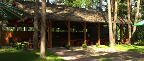 A wooden pavilion with a covered seating area, surrounded by trees and a gravel path.