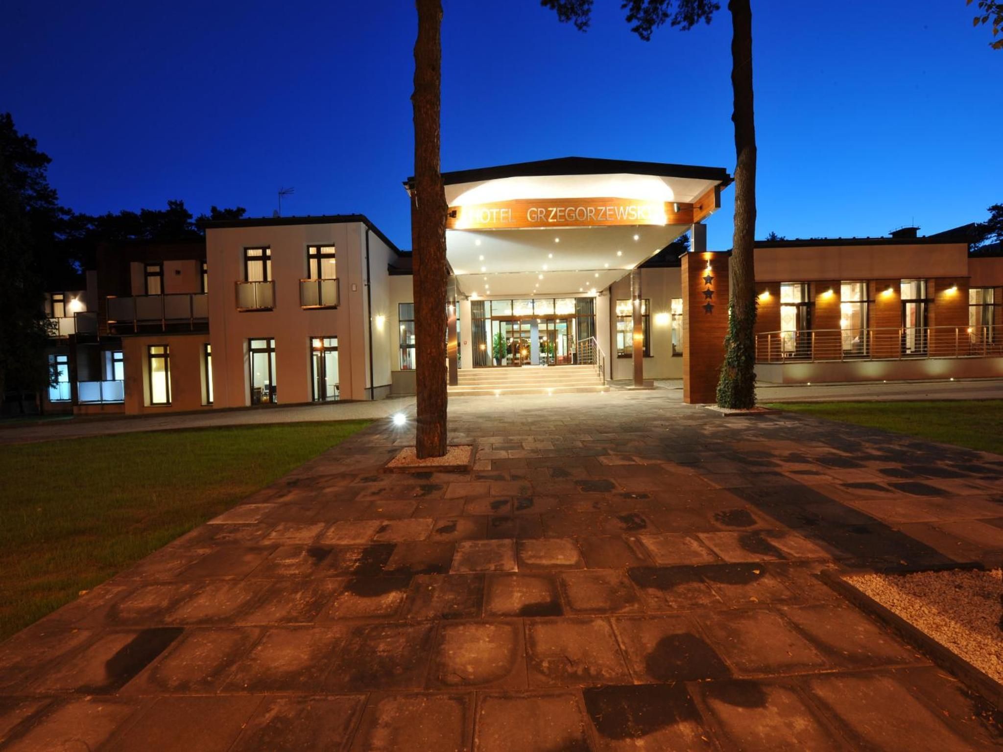 A modern hotel entrance with a covered walkway, a clear sky, and a well-lit facade.