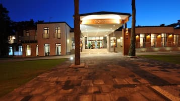 A modern hotel entrance with a covered walkway, a clear sky, and a well-lit facade.