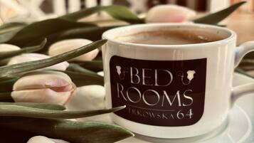 Una taza blanca con la leyenda 'BED ROOMS' sobre un platito, rodeada de tulipanes rosados.